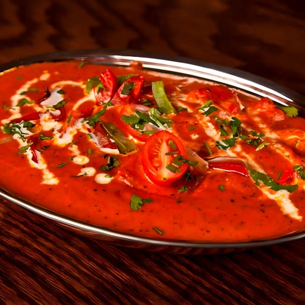 Vibrant Indian curry with a rich red sauce, garnished with fresh herbs, cream, and sliced tomatoes.