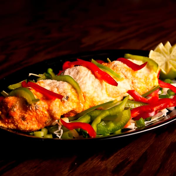 Indian dish with paneer, red and green bell peppers, and a lime wedge on a dark plate.