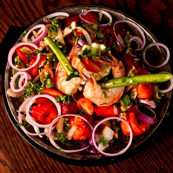 Sizzling Indian shrimp and chicken tikka with onions, tomatoes, and green chilies on a dark platter.