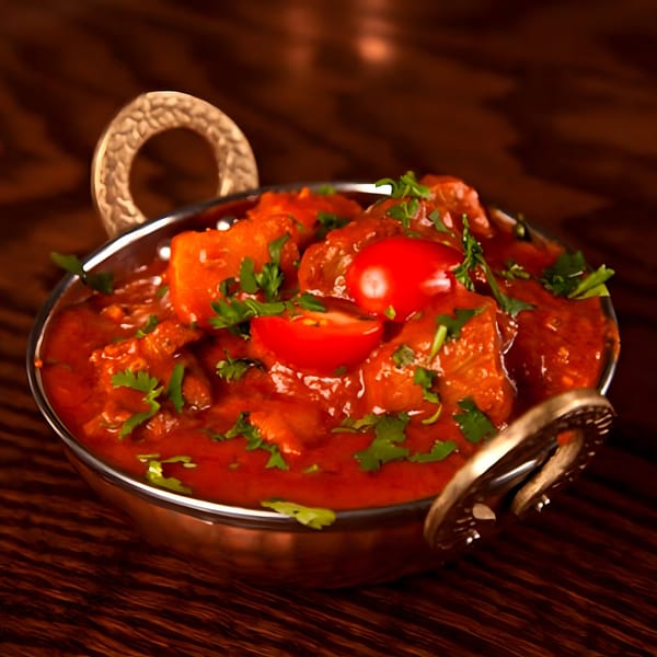 Indian chicken curry in a copper karahi, garnished with fresh cilantro and cherry tomatoes.