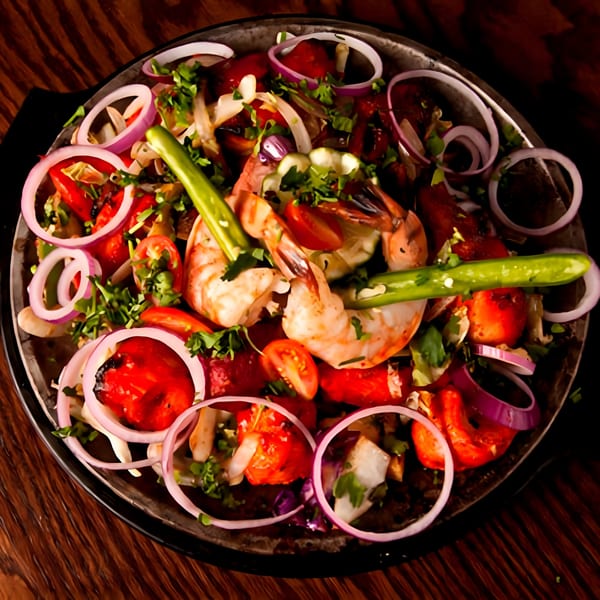 Indian shrimp and chicken tikka with onions, tomatoes, and green chilies in a dark pan.