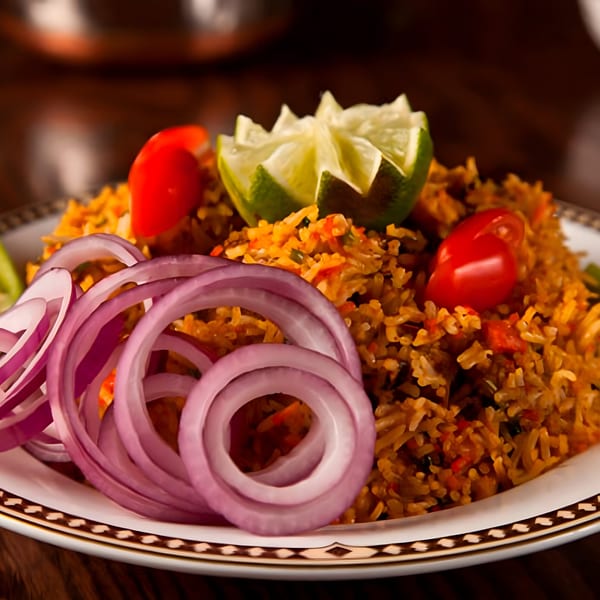 Indian biryani rice dish, garnished with red onion rings, cherry tomatoes, and a lime wedge.