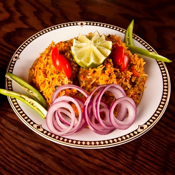Indian biryani with lime, cherry tomatoes, okra, and red onion rings on a white plate.