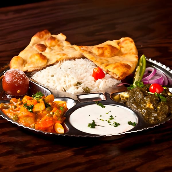 A Swagat Fine Indian Cuisine thali with rice, naan, gulab jamun, vegetable curry, saag, and raita.