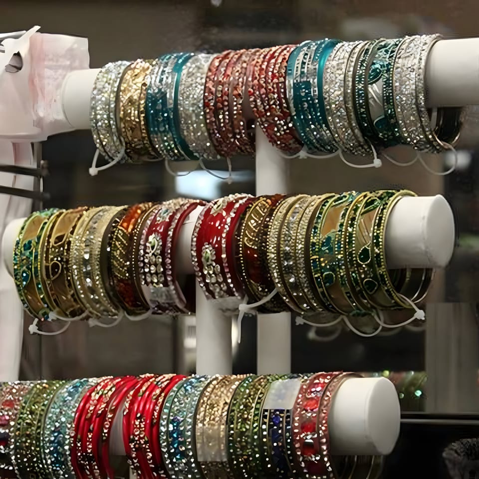 Rows of colorful, ornate Indian bangles displayed on white stands, reflecting light.