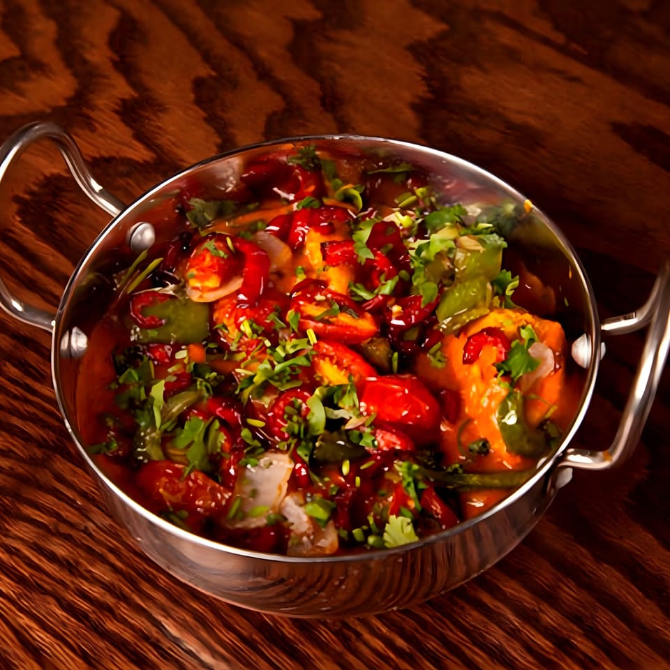 Indian chili chicken or paneer in a metal karahi, garnished with fresh cilantro on a wooden table.